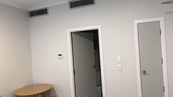 A room with a door, a table with a chair, and a toilet visible through the door.