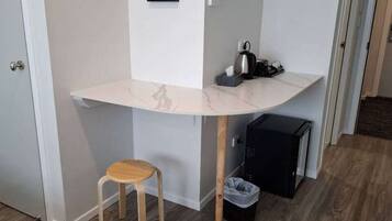 A compact room with a white marble desk, a small wooden stool, a black trash bin, and a black storage unit.