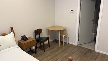 Habitación de hotel con cama, mesita de noche con teléfono, una silla, una mesita pequeña y una puerta que da al baño.