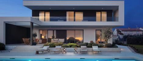 A modern two-story house with a swimming pool, outdoor seating, and a well-maintained garden.
