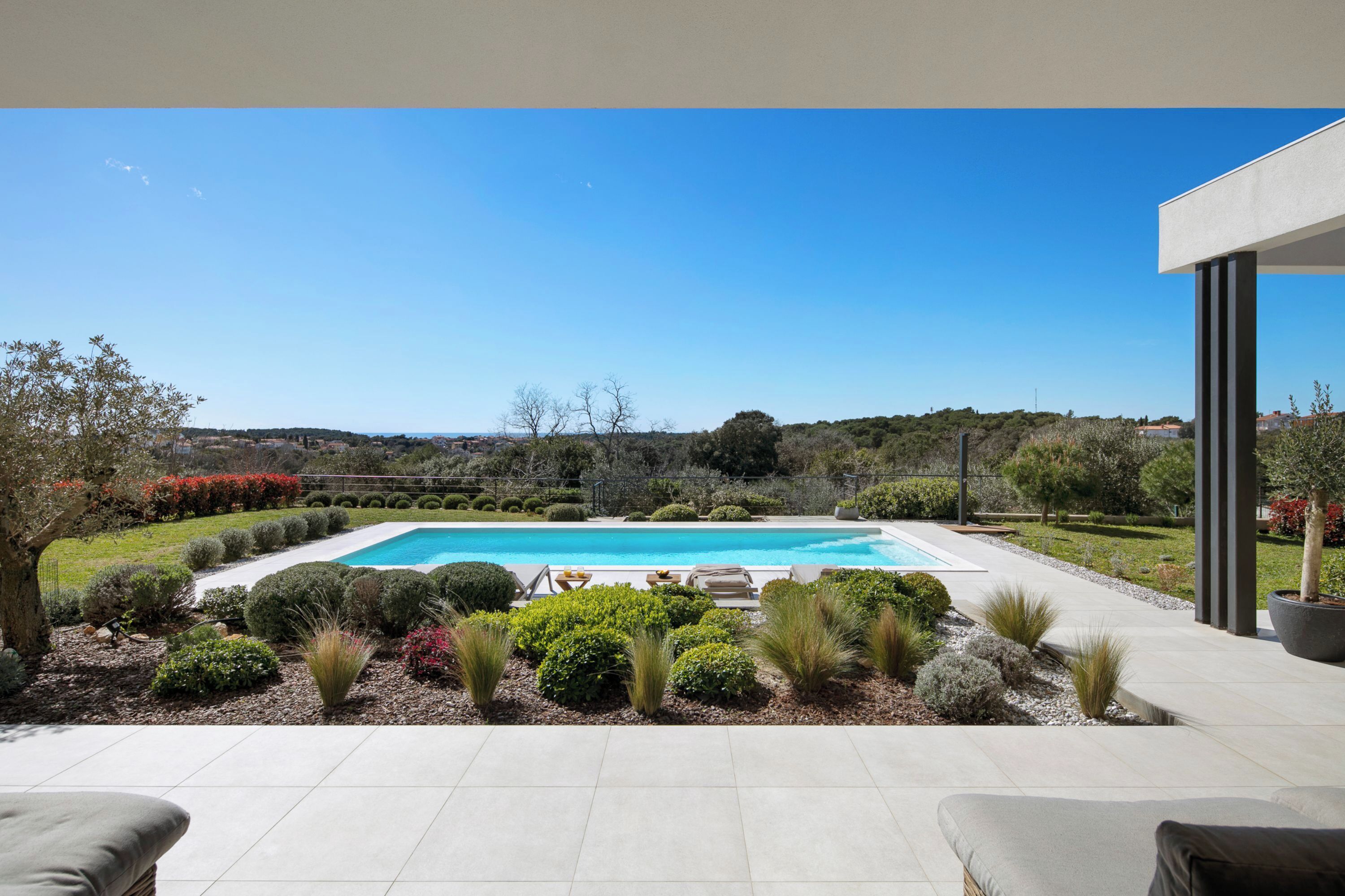 A swimming pool with a view of the countryside, surrounded by well-maintained gardens and a modern outdoor seating area.