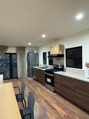 Eine moderne Küche mit Essbereich, Holzschränken, einem Edelstahl-Kühlschrank und einem eingebauten Backofen.