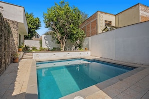 A rectangular swimming pool with a tiled deck surrounding it.