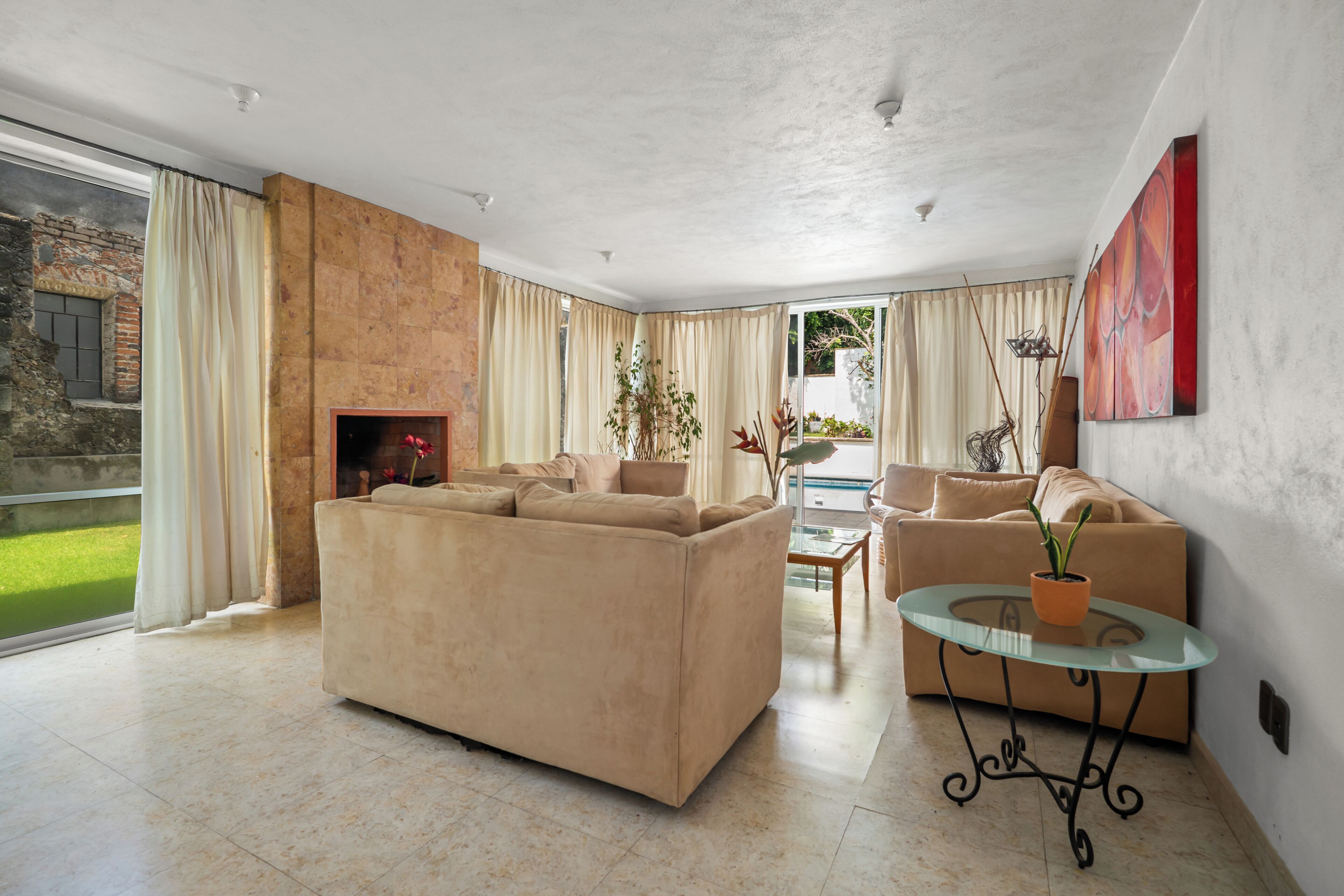 A spacious living room with a beige sofa, a glass coffee table, and a fireplace.