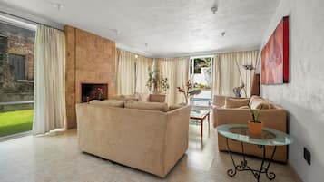 A spacious living room with a beige sofa, a glass coffee table, and a fireplace.
