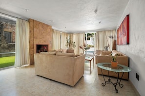 A spacious living room with a beige sofa, a glass coffee table, and a fireplace.