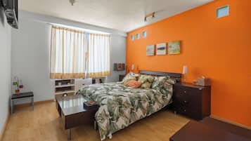 A bedroom with a bed, a bedside table, a dresser, a window with curtains, and a wall with three small pictures.