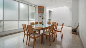 A modern dining area with a glass table surrounded by wooden chairs, a vase with flowers, and a potted plant.
