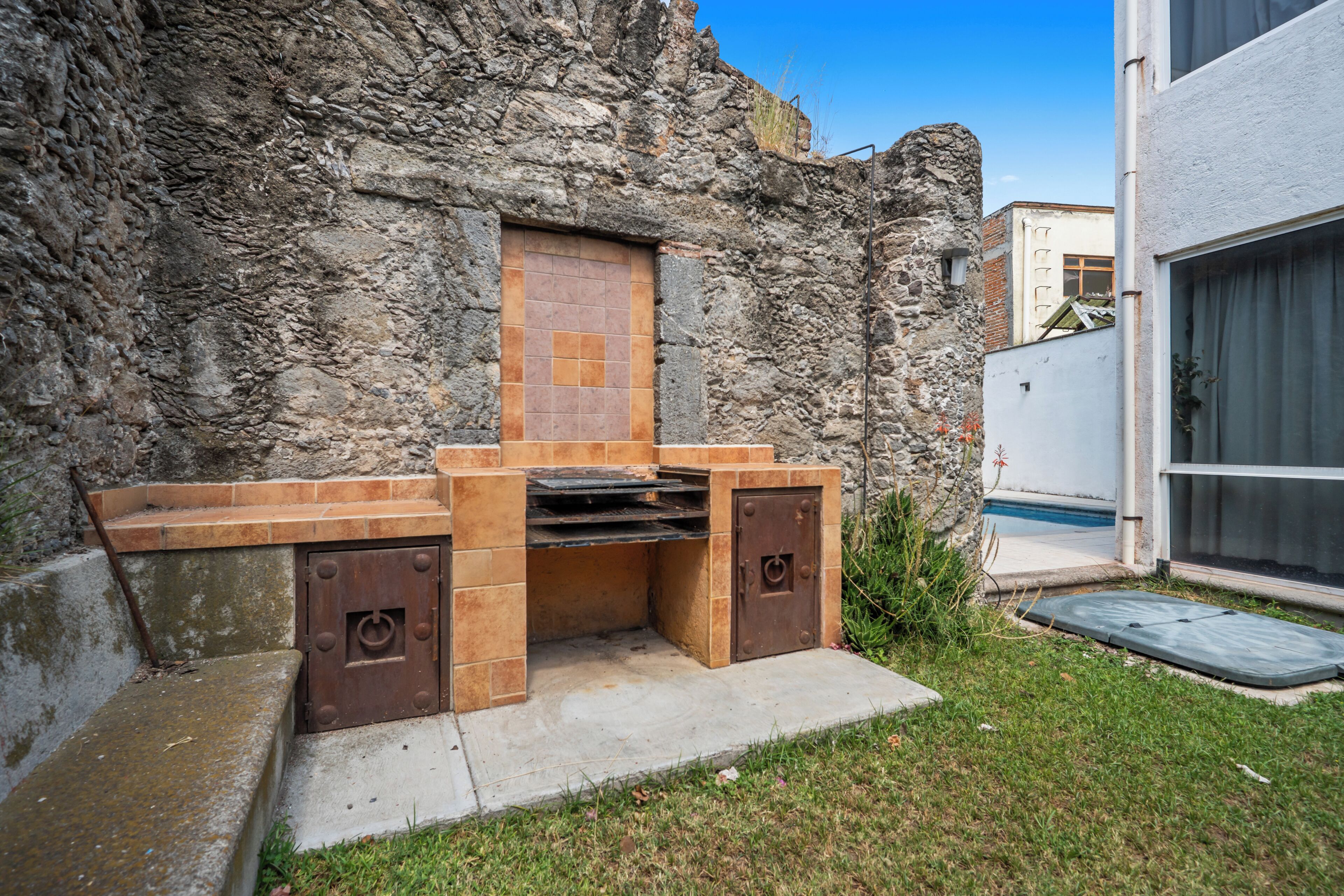 Una cocina exterior con un muro de piedra de fondo, un salpicadero de azulejos y un horno empotrado.
