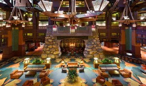 A spacious lobby with a central seating area, stone pillars, and a high ceiling with hanging lamps.
