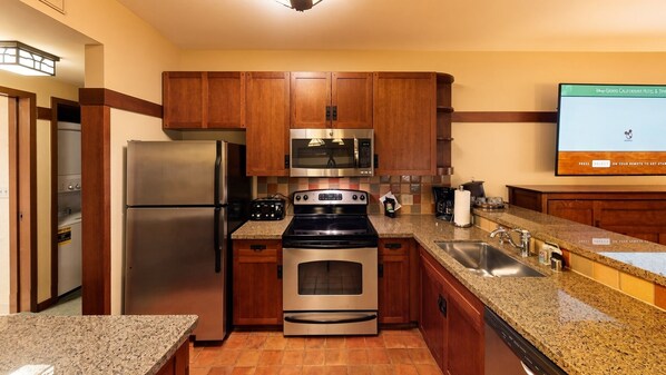 A modern kitchen with stainless steel appliances, wooden cabinets, granite countertops, and a built-in dishwasher.