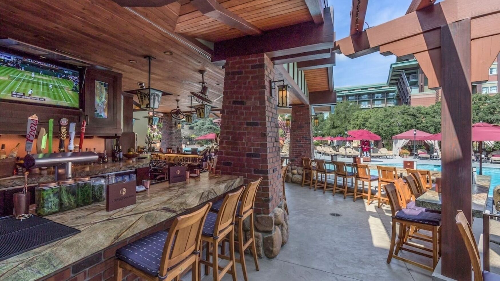 An outdoor bar area with a poolside view, wooden chairs, and a bar counter.