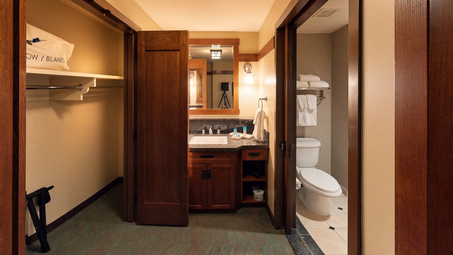 A hotel bathroom with a wooden vanity, a sink, a mirror, and a toilet.