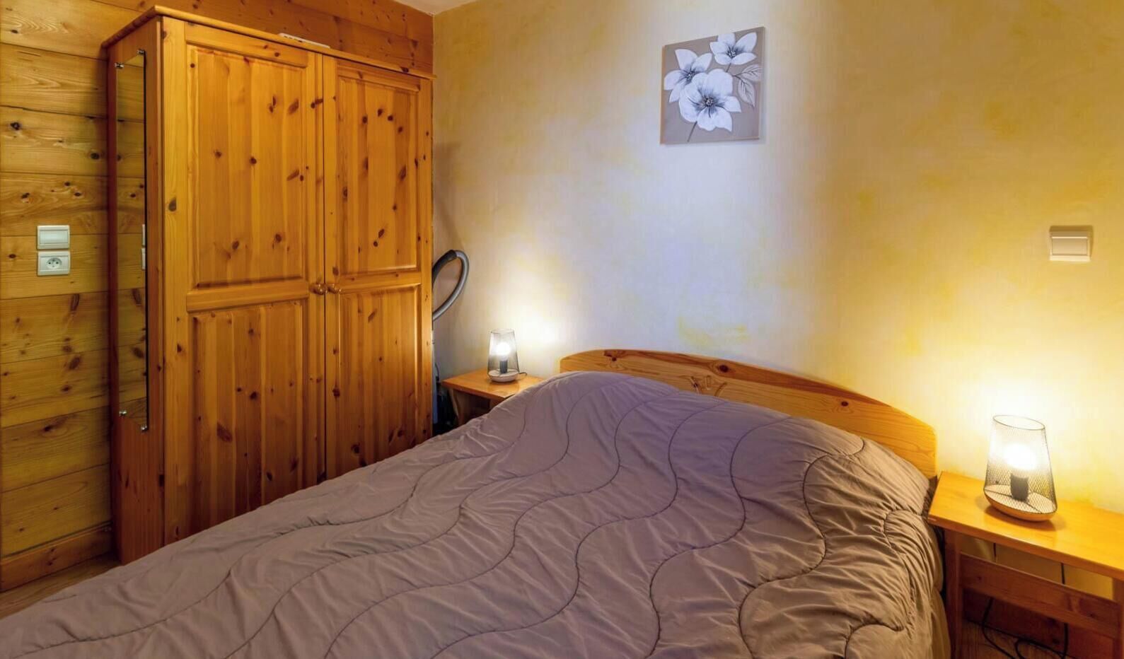 A bedroom with a bed, wooden wardrobe, two bedside lamps, and a wall-mounted light fixture.