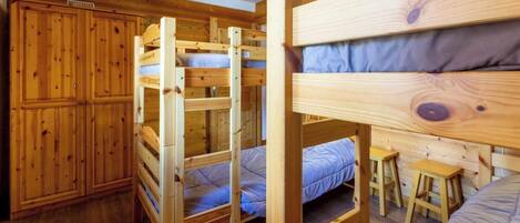 Quarto com beliche, guarda-roupa de madeira e pequena escrivaninha com banquinhos.