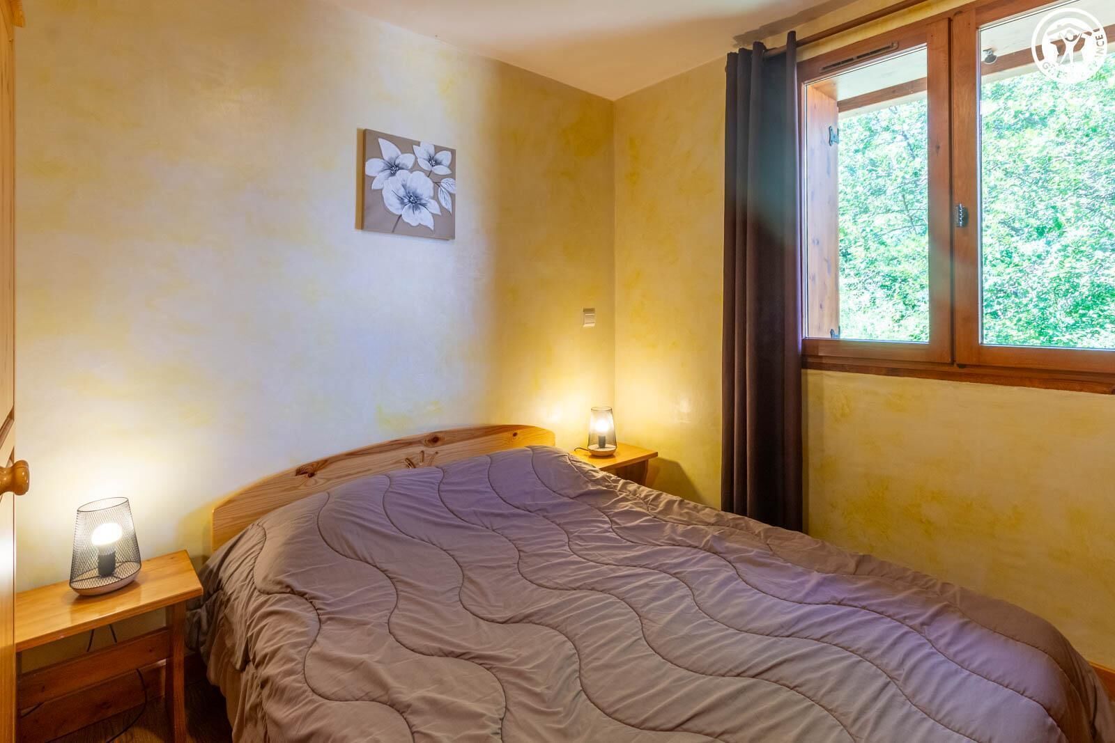Une chambre à coucher avec un lit, une lampe de chevet, un tableau accroché au mur et une fenêtre avec des rideaux.