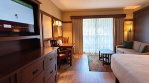A hotel room with a bed, a desk, a chair, a television, and a window with curtains.
