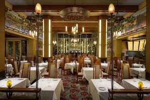 Een restaurant met meerdere tafels, stoelen en hangende lampen.
