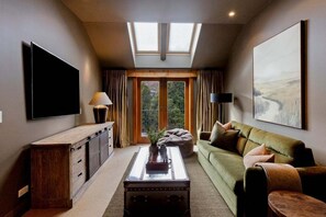 Ein modernes Wohnzimmer mit Flachbildfernseher, einer Couch, einem Couchtisch und einem großen Fenster mit Vorhängen.