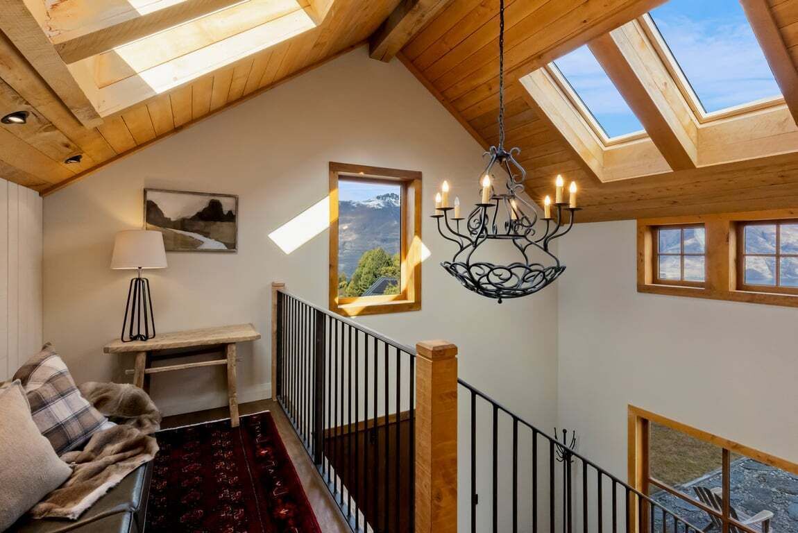 A high-ceilinged room with skylights, a chandelier, a wooden bench, a sofa, and a view of the outdoors.