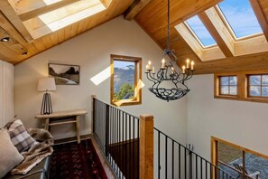 A high-ceilinged room with skylights, a chandelier, a wooden bench, a sofa, and a view of the outdoors. - Altitude Vista-Front row Seat to Queenstown's Finest Views (Ben Lomond)
