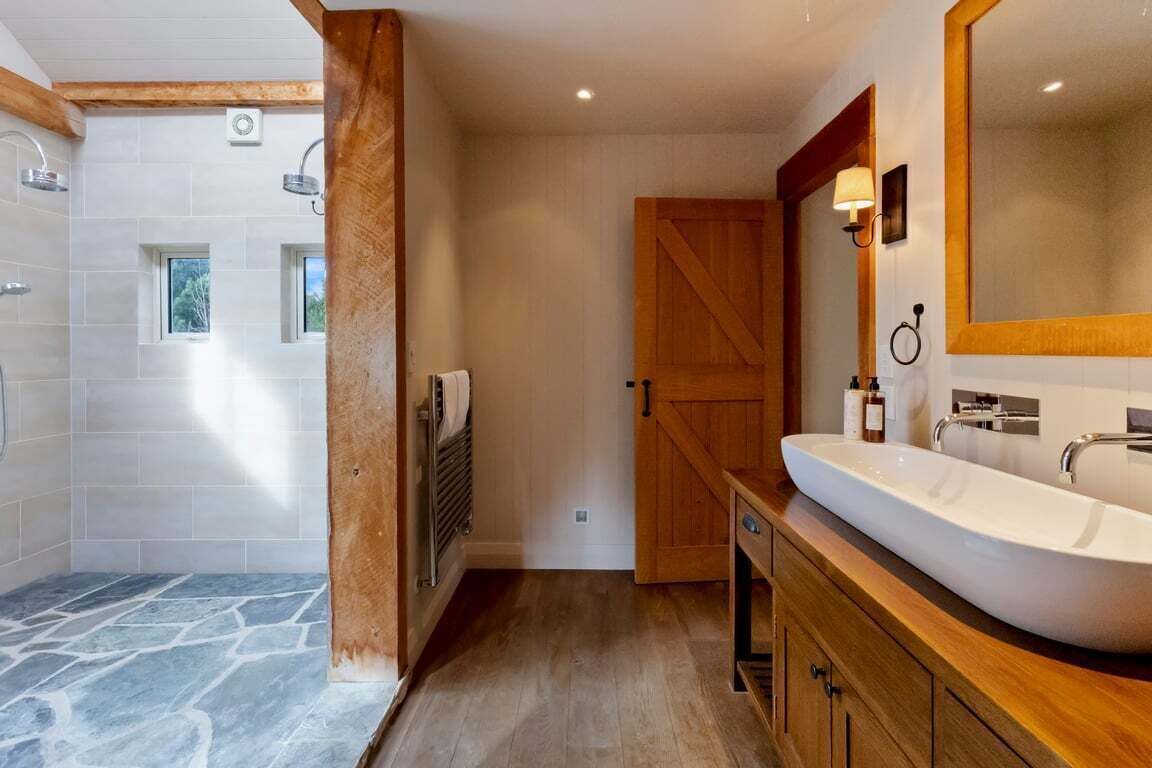 A bathroom with a stone shower, wooden vanity, and a large mirror.