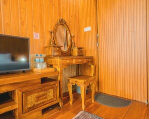 A wooden room with a television, a vanity with a mirror, and a small stool.