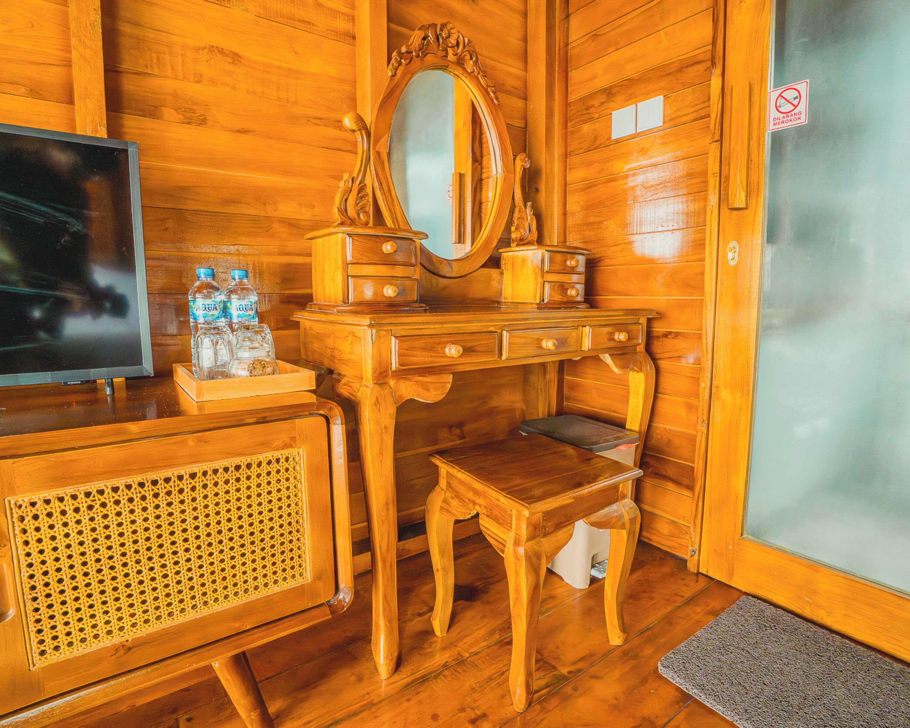 Une pièce en bois avec une télévision, une commode en bois dotée de tiroirs, un miroir et un petit tabouret.