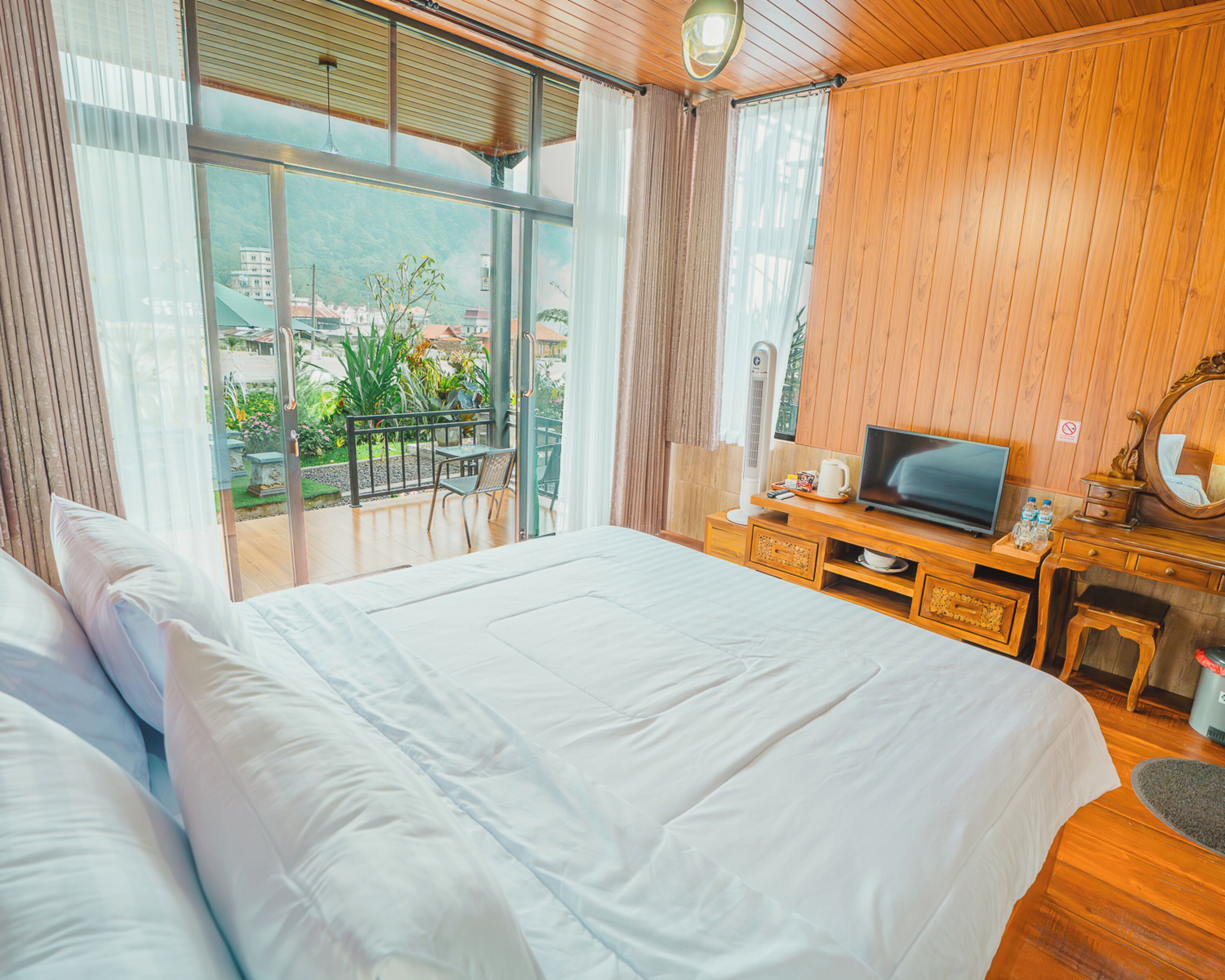 A hotel room with a large bed, a television, a desk with a chair, and a view of the outdoors.