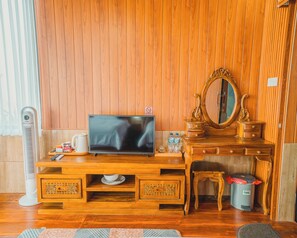 A wooden room with a television, a mirror, a cabinet, and a trash bin.