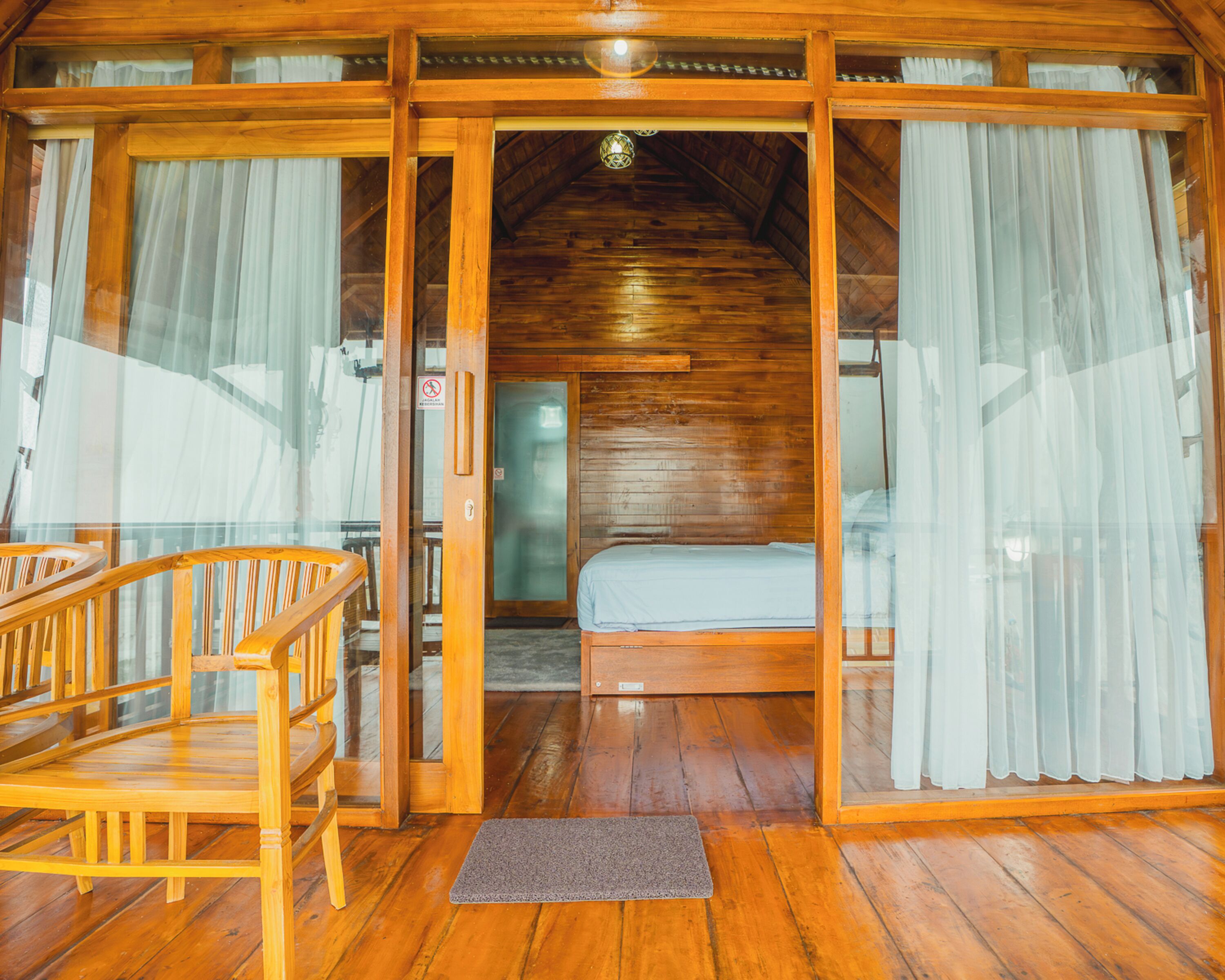 A wooden cabin interior with a bed, a chair, and a door leading to another room.