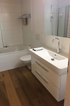 A bathroom with a bathtub, toilet, sink, and wooden flooring. - Chalet Lohner Appartement/Fewo, Bad, WC, 2 Schlafräume 3-Zimmerwohnung by Interhome (Adelboden)