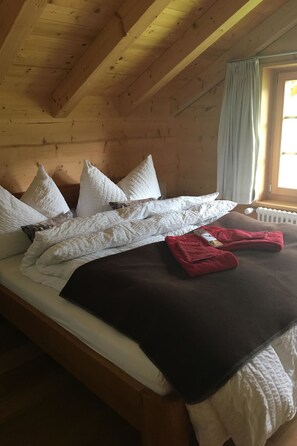 A wooden cabin room with a bed, pillows, a blanket, and a window with curtains. - Chalet Lohner Appartement/Fewo, Bad, WC, 2 Schlafräume 3-Zimmerwohnung by Interhome (Adelboden)