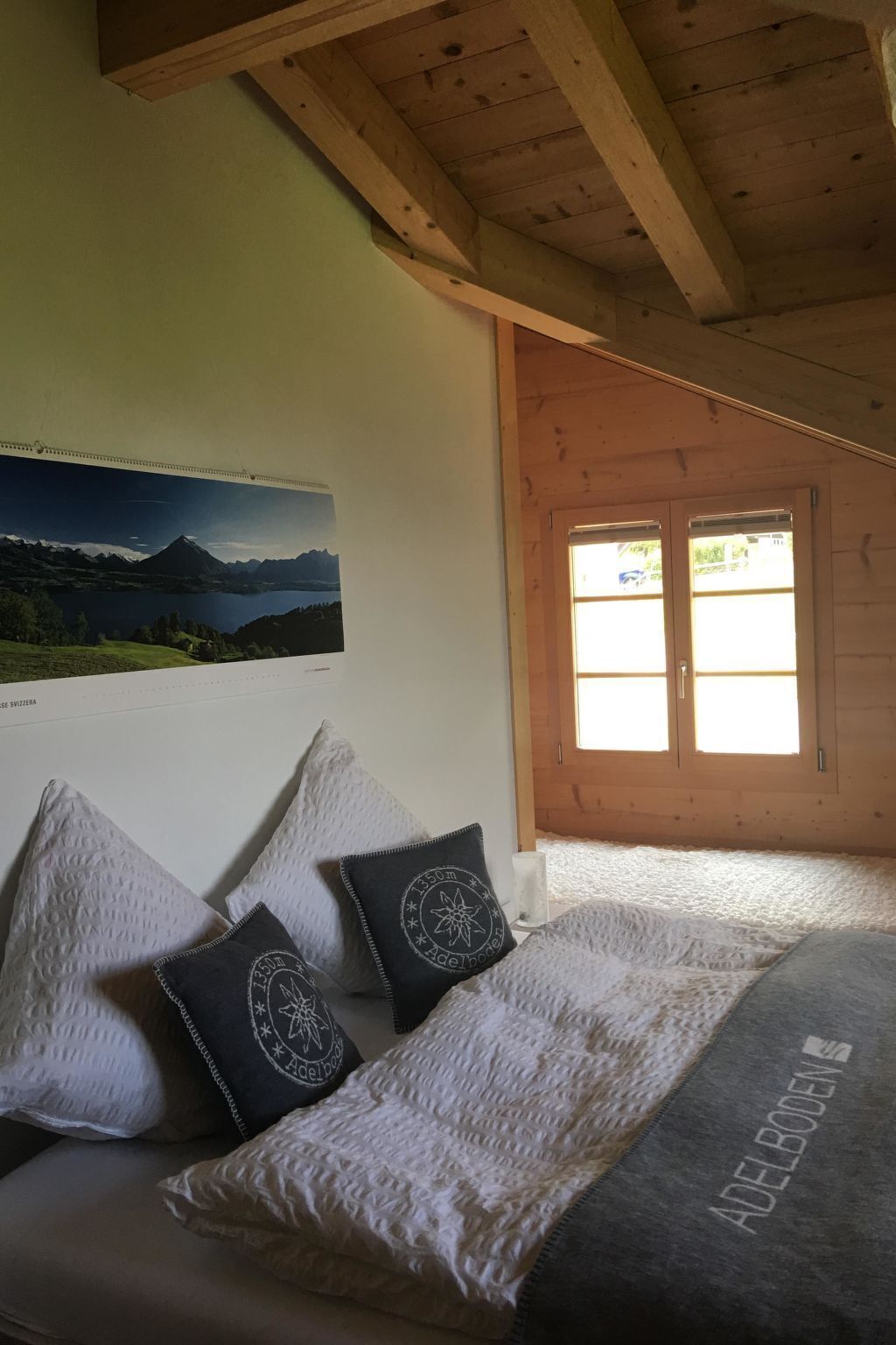 Una camera da letto con un letto, cuscini, un quadro appeso al muro e un soffitto in legno.