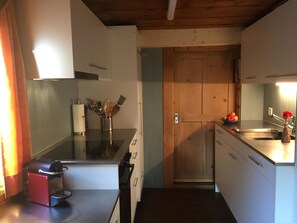 A compact kitchen with a wooden door, stainless steel appliances, and a fruit bowl on the counter. - Sunnebühl Appartement/Fewo, Bad, WC, 3 Schlafräume Ferienhaus 5.5-Zimmerwohnung by Interhome (Adelboden)