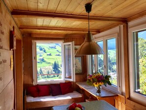 A wooden interior with a bench, a table with fruit, and a view of green fields through windows. - Sunnebühl Appartement/Fewo, Bad, WC, 3 Schlafräume Ferienhaus 5.5-Zimmerwohnung by Interhome (Adelboden)
