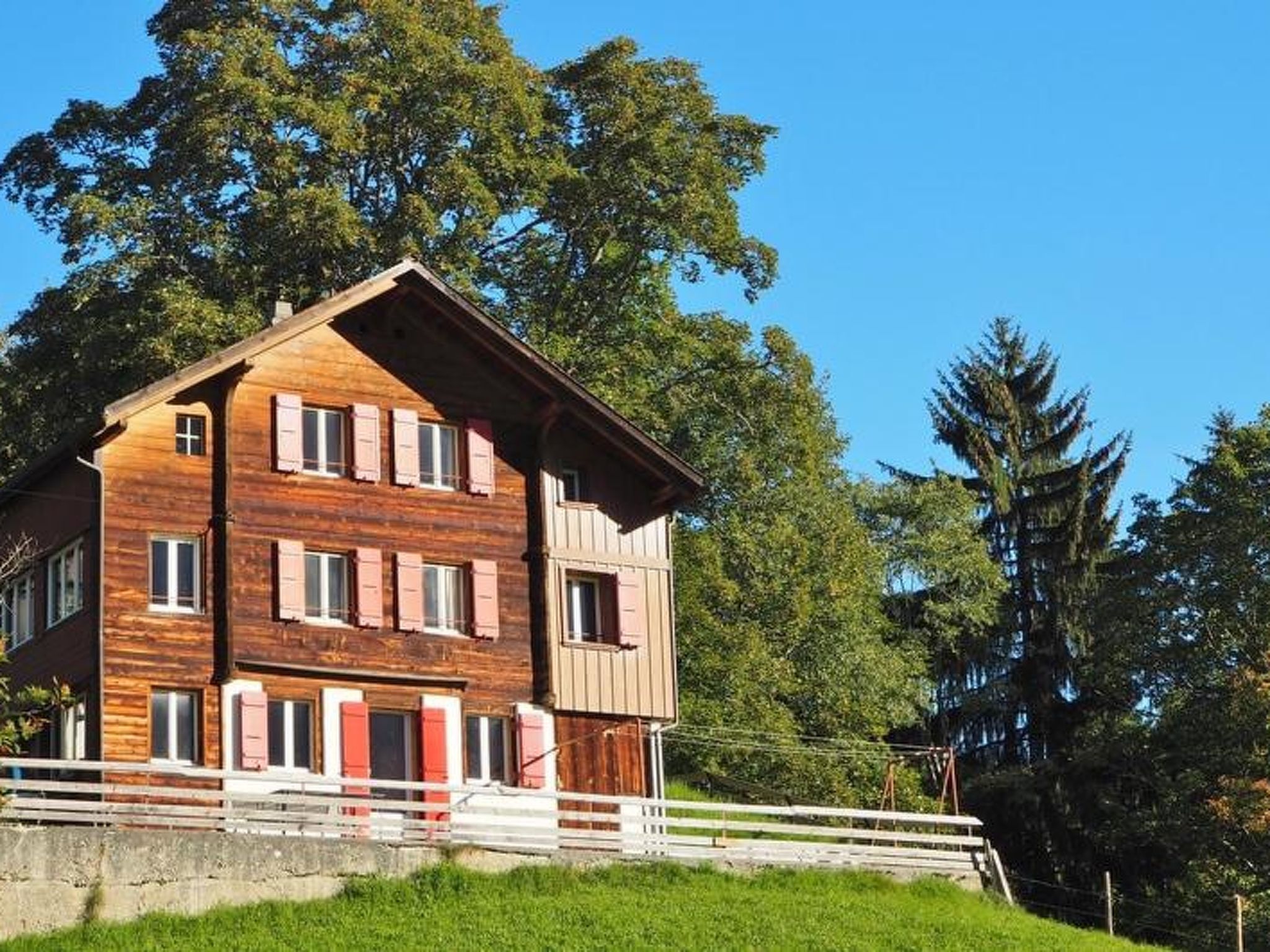 Een houten huis met twee verdiepingen en een balkon, omringd door bomen.