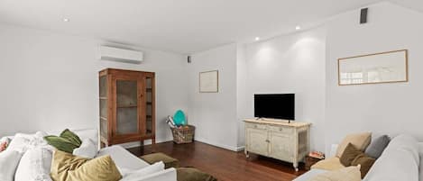 A living room with a white sofa, a wooden cabinet, a television, and a framed picture on the wall.