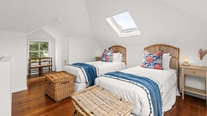 A bedroom with two beds, a skylight, a wicker chest, and a wooden nightstand. - Willowbank Homestead (Greater Geelong)