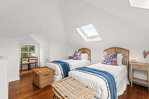 Ein Schlafzimmer mit zwei Betten, einem Oberlicht, einer Korbschublade und einem Nachttisch aus Holz.