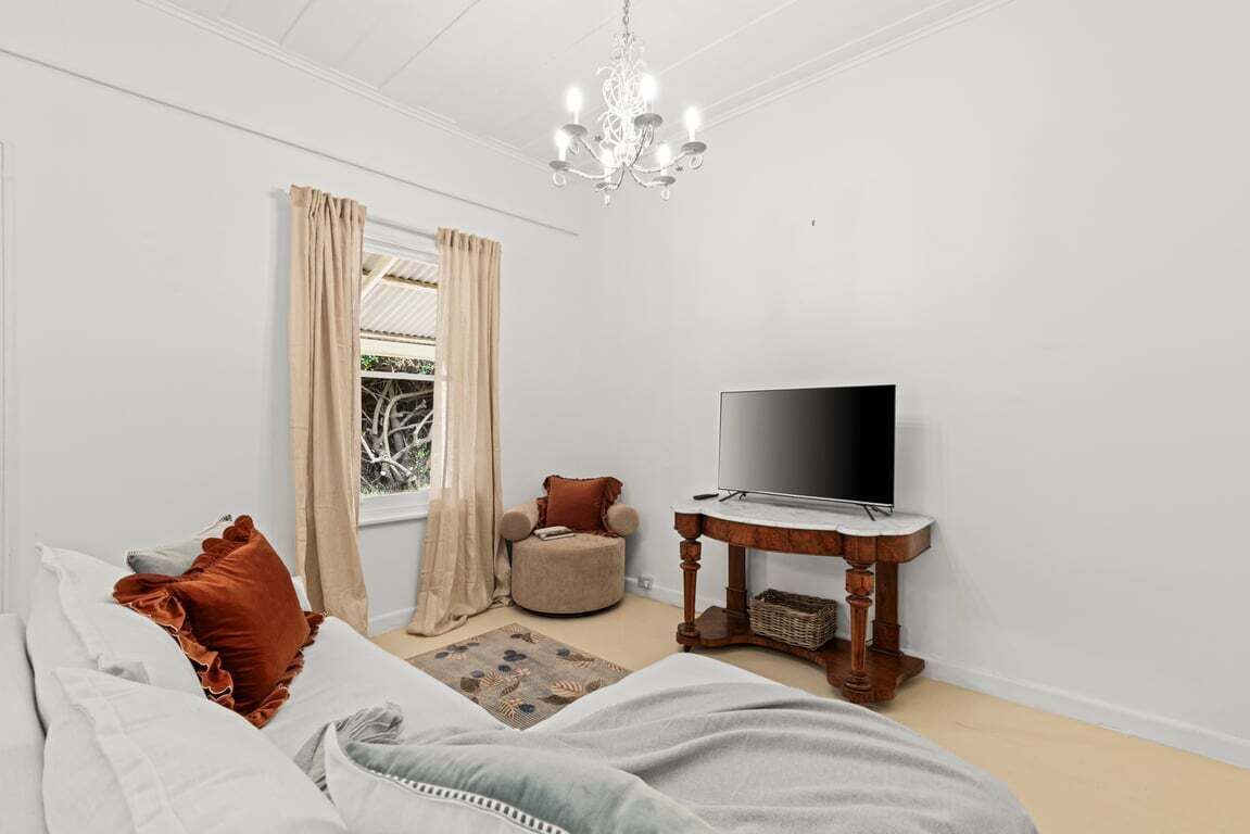Un dormitorio con cama, televisión, mesita de madera, ventana con cortinas y candelabro.