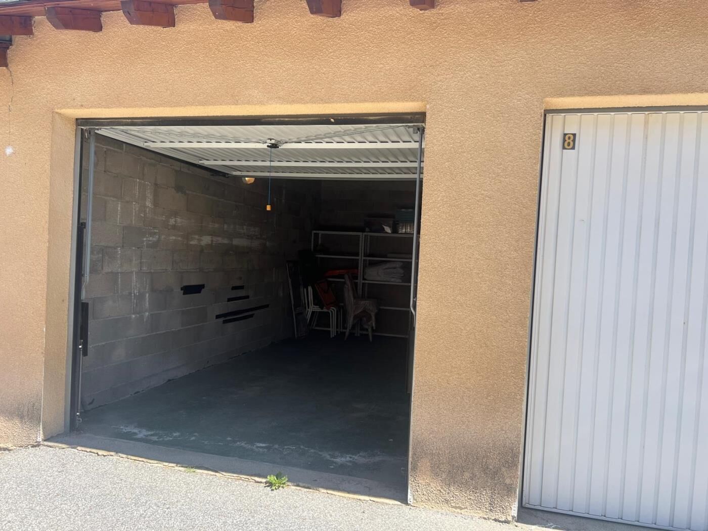 A garage with a closed door on the right and an open door on the left, revealing a storage area with shelves and folded chairs.