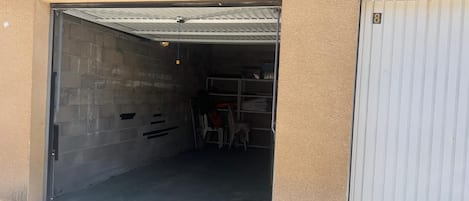 A garage with a closed door on the right and an open door on the left, revealing a storage area with shelves and folded chairs.