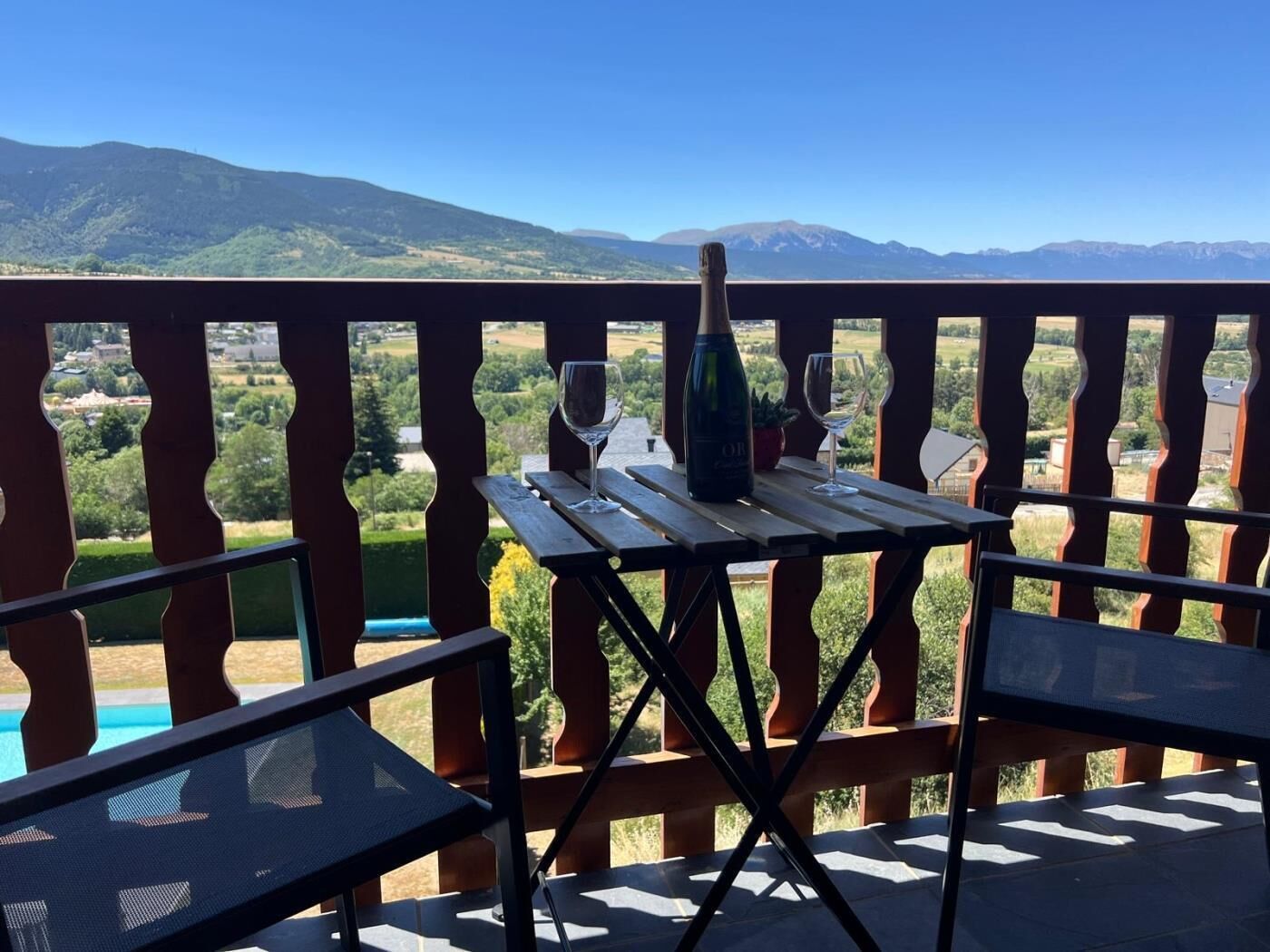 Un balcón con una mesa dispuesta para dos personas, con vistas a un paisaje montañoso.
