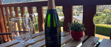 A bottle of CAVA wine and two glasses on a wooden table with a view of mountains.