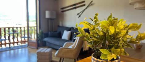 A living room with a sofa, a small table with a potted plant, and a balcony with a railing.