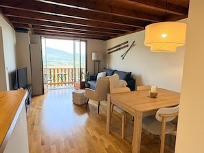 A room with a wooden floor, a sofa, a dining table, and a television. There is a balcony with a view of the outdoors. - Apartment 5 People with pool in Saillagouse (Saillagouse)