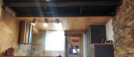 Une cuisine avec un plafond en bois, une rambarde en métal noir et un mur en pierre.