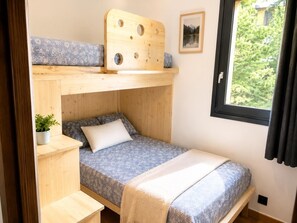 A compact room with a bunk bed, a small bedside table, a potted plant, and a window with a view of greenery. - Bolquère Ski Slopes Apartment (Bolquere)