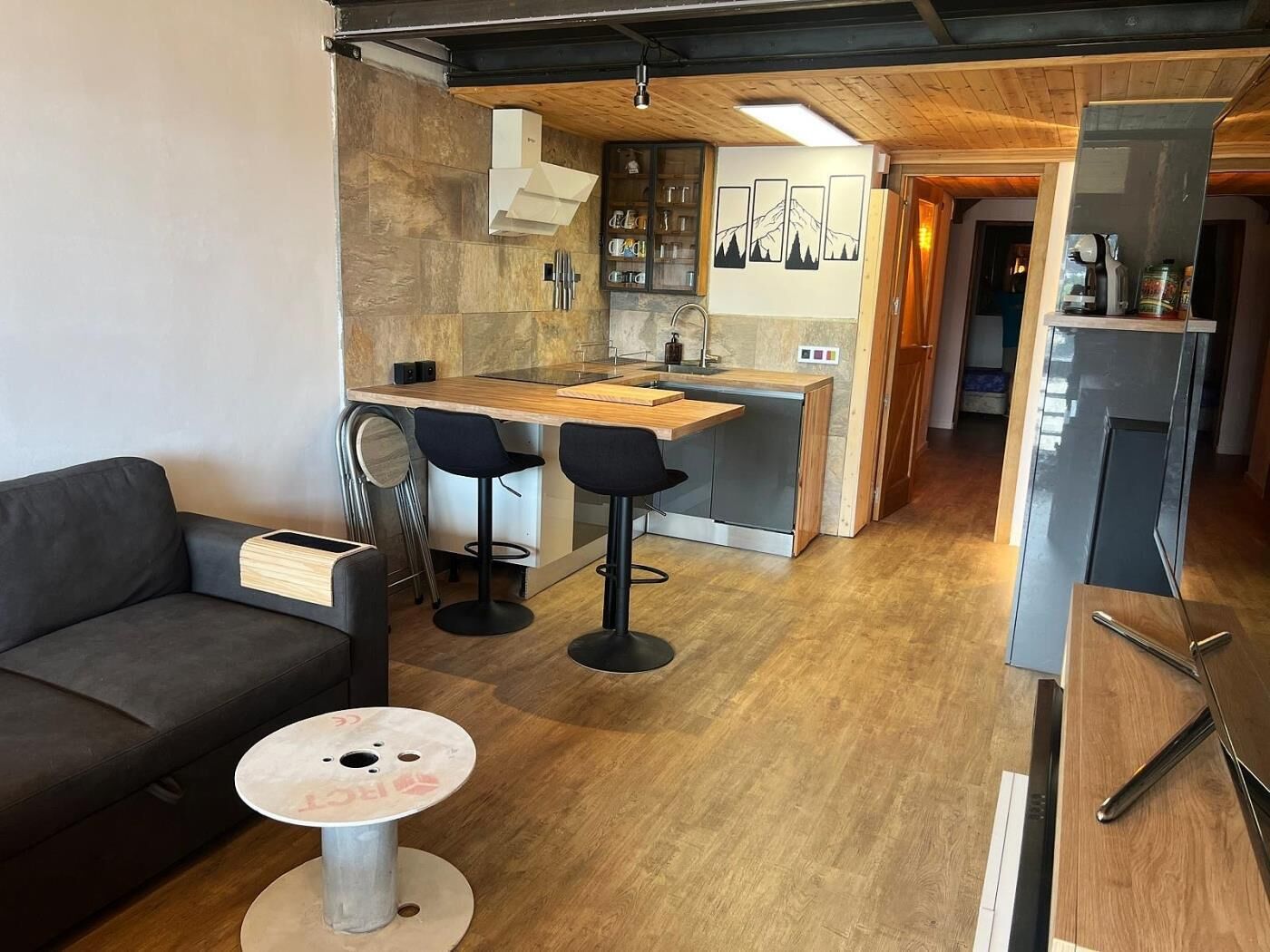 A compact living space with a kitchenette, a dining area with two bar stools, a small round table, and a sofa.